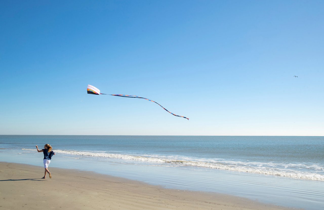 Woman trots along the beach, flying a kite