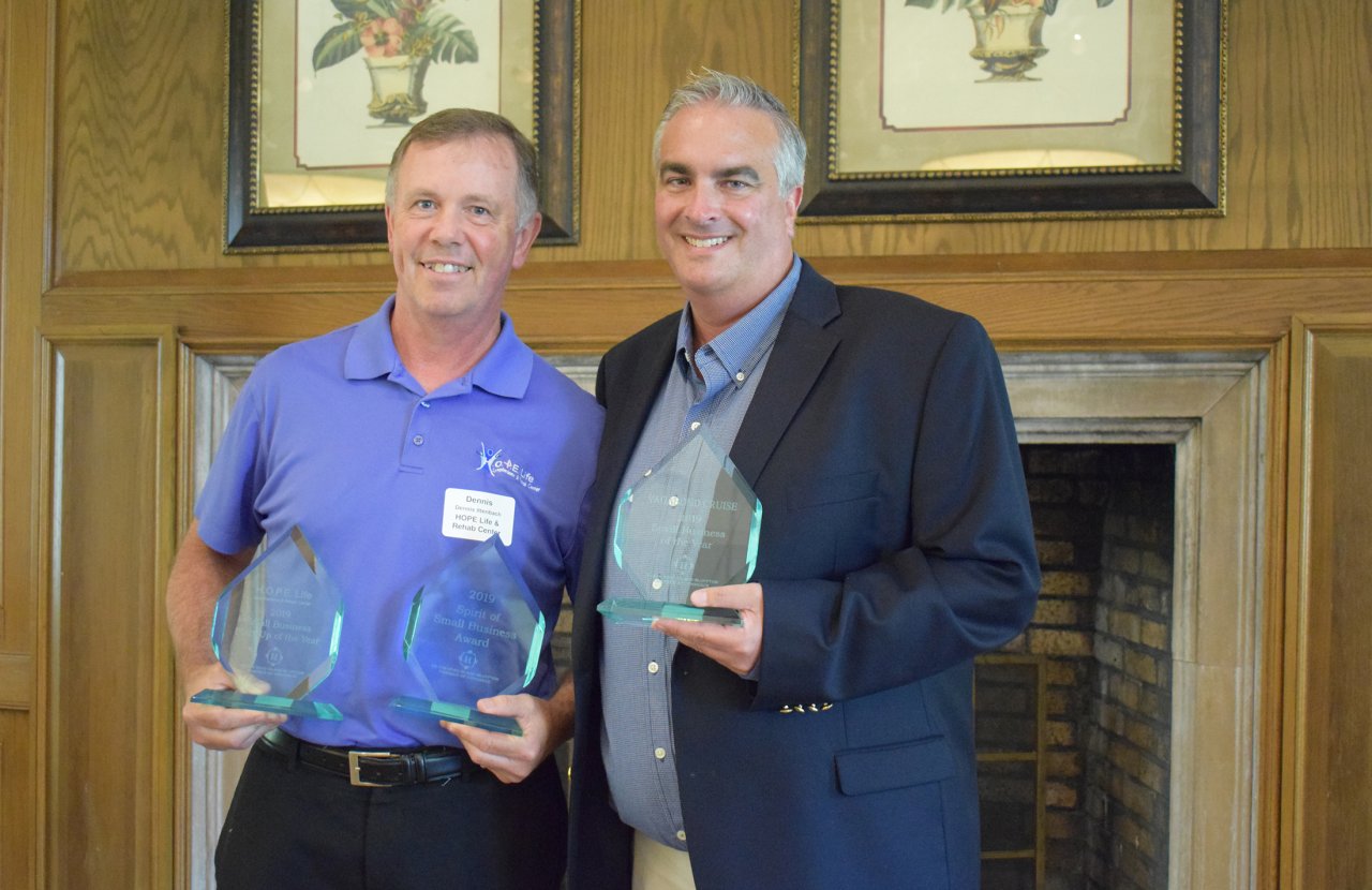 two middle aged men hold glass awards and smile